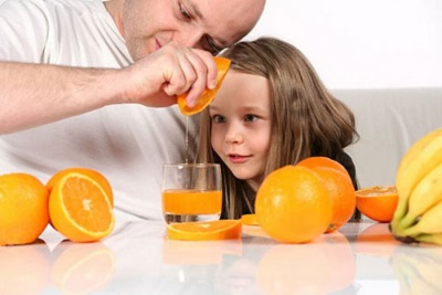 Jugo fresco de naranja es preparado por un niño con papá.