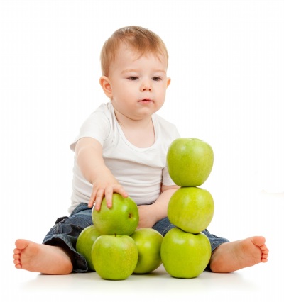 The infant builds a tower of green apples