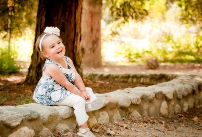 Niña de 2 años se sienta en un tronco.